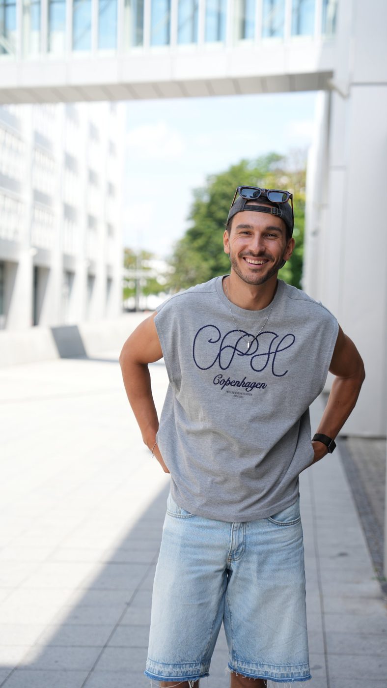 Frederic lachend mit Cap und Sonnenbrille im grauen Copenhagen-Shirt in der Stadt