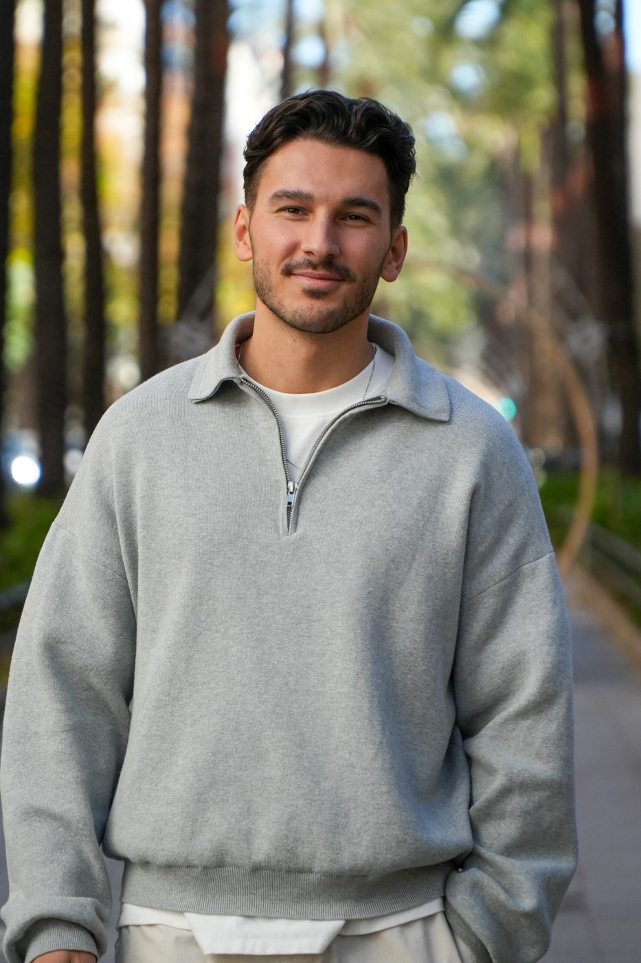 Frederic lächelnd im grauen Pullover in einer Palmenallee